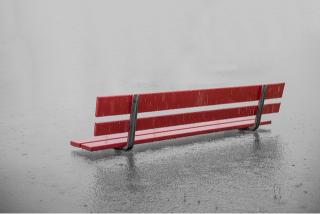 A red park bench surrounded by water