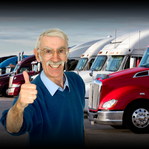 An older male business owner in his 60s standing in a parking lot with a line of heavy trucks in the background, giving a thumbs up gesture, representing a business owner who has secured favorable rates for his commercial auto insurance in Montana.