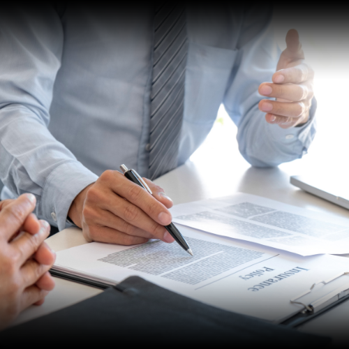 An insurance agent, visible from the torso up, explains a policy at a desk while a prospective client listens intently with clasped hands. This image represents the flexible commercial auto insurance policies available for business owners in Montana.