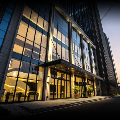 View from ground level looking up at a modern office building with full glass facade at dusk, representing commercial property.