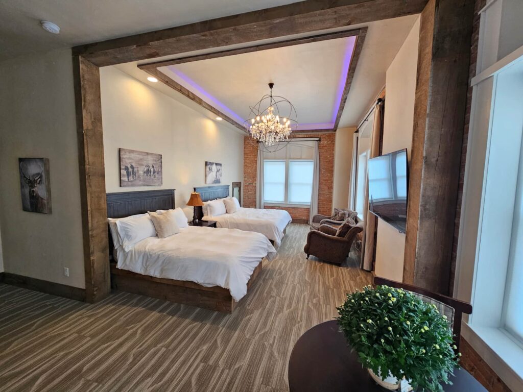 Executive Studio Suite at Eaglescape Suites & Event Center with a king and queen bed, 500 sq ft of space, 12-foot ceilings, crystal chandelier, tiled shower, custom double-sink vanity, lounge seating, and a kitchenette in a luxurious downtown setting